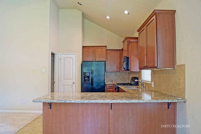 kitchen with light stone countertops, brown cabinets, a peninsula, and black refrigerator with ice dispenser