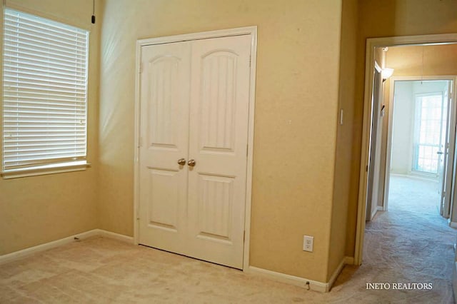 unfurnished bedroom featuring a closet, light carpet, and baseboards