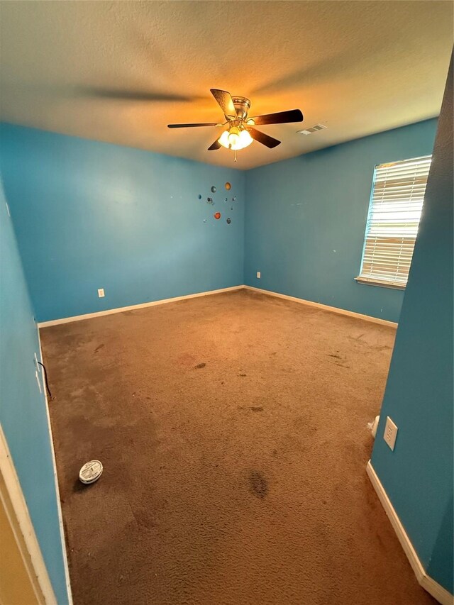 unfurnished room featuring carpet, visible vents, a ceiling fan, baseboards, and a textured ceiling