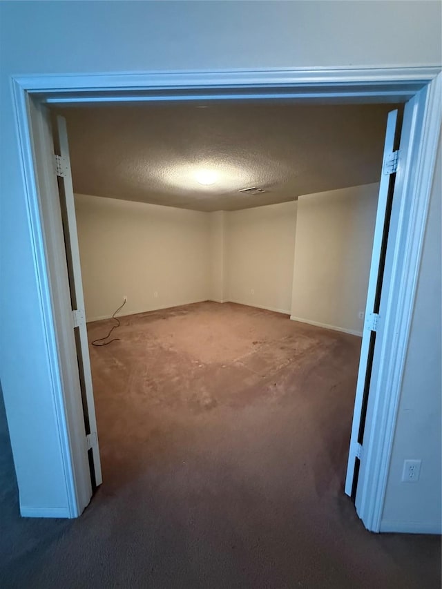 basement featuring baseboards, a textured ceiling, and carpet