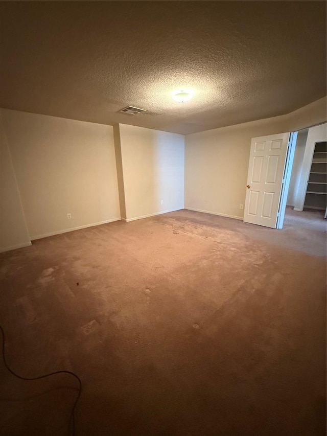 finished below grade area featuring visible vents, baseboards, a textured ceiling, and carpet flooring