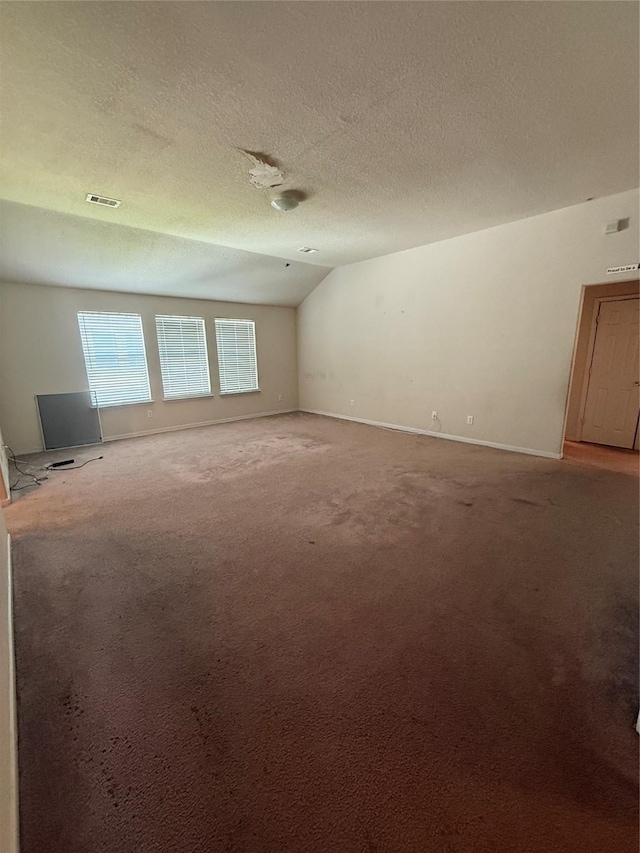 carpeted empty room with visible vents, a textured ceiling, baseboards, and vaulted ceiling