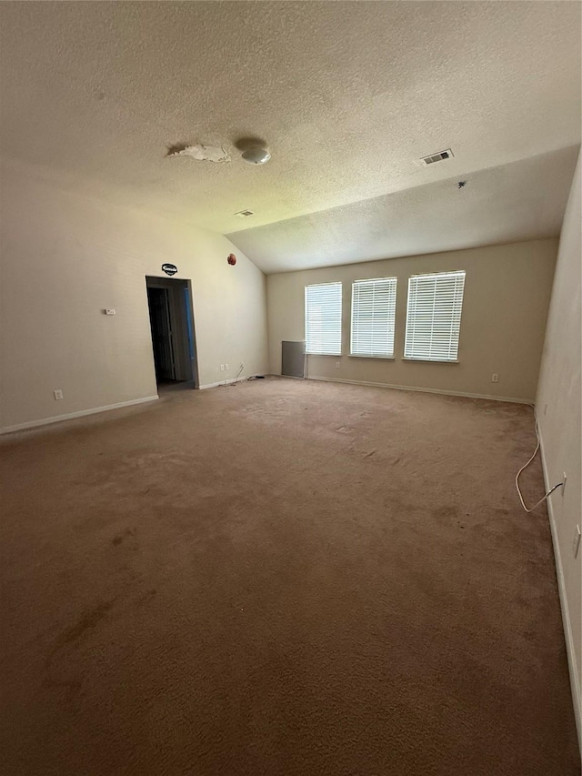 carpeted spare room with baseboards, visible vents, a textured ceiling, and lofted ceiling