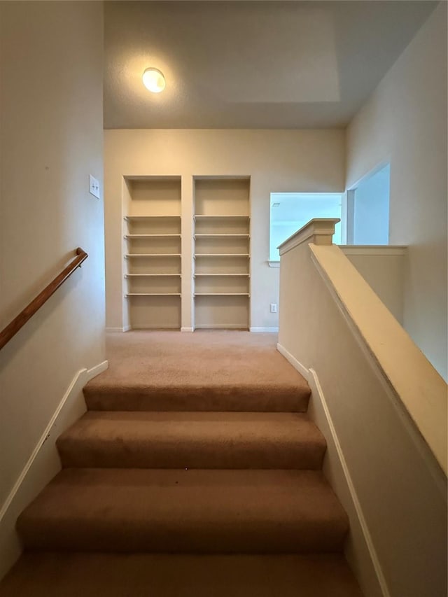 staircase featuring built in shelves, baseboards, and carpet floors