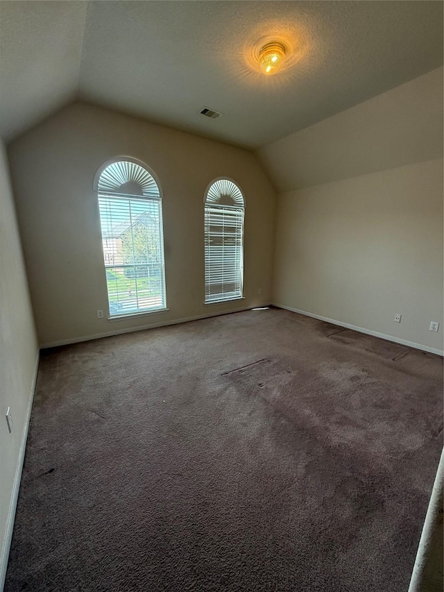 interior space featuring visible vents, a textured ceiling, baseboards, and vaulted ceiling