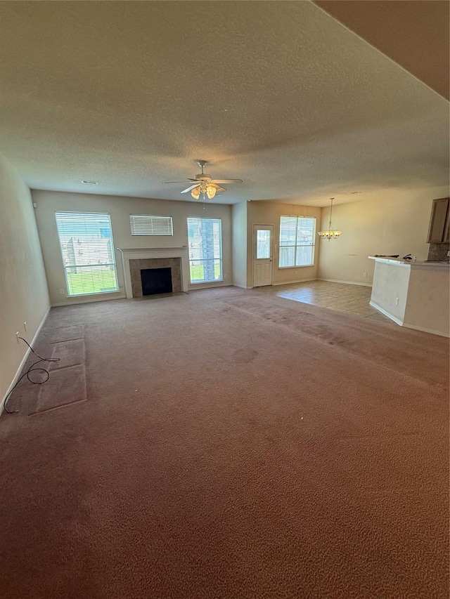 unfurnished living room featuring baseboards, a fireplace, a textured ceiling, ceiling fan with notable chandelier, and light colored carpet