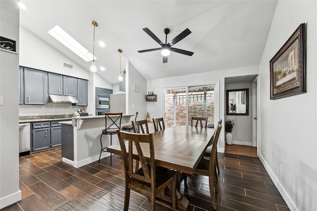 dining room featuring visible vents, wood finish floors, baseboards, ceiling fan, and vaulted ceiling with skylight