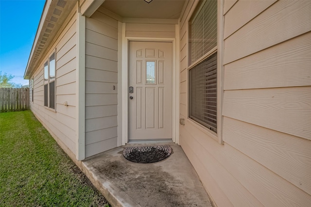 view of exterior entry with a yard and fence