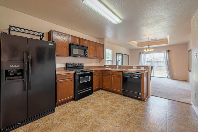 kitchen with a notable chandelier, black appliances, a sink, a peninsula, and a raised ceiling