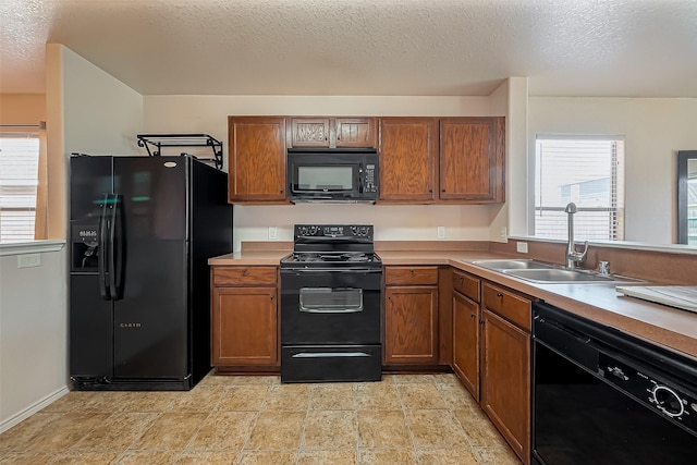 kitchen featuring black appliances, a sink, a textured ceiling, brown cabinetry, and light countertops