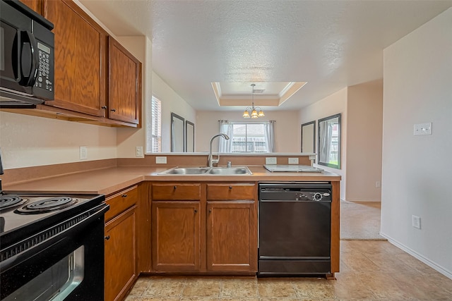 kitchen with brown cabinets, black appliances, a sink, a peninsula, and a raised ceiling