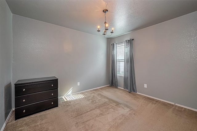 empty room featuring a chandelier, a textured ceiling, baseboards, and carpet floors