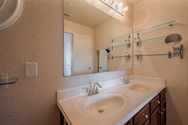 bathroom featuring double vanity, visible vents, a textured wall, and a sink