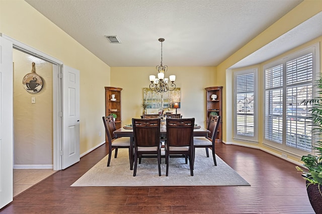 dining area with visible vents, a textured ceiling, wood finished floors, baseboards, and a chandelier