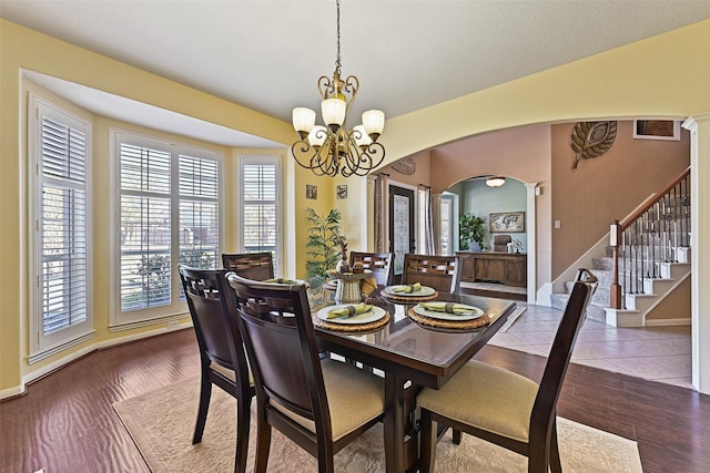 dining space featuring stairs, dark wood-type flooring, arched walkways, and a chandelier