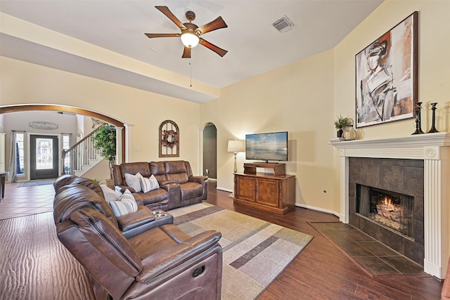 living area with visible vents, a fireplace, arched walkways, a ceiling fan, and dark wood-style flooring