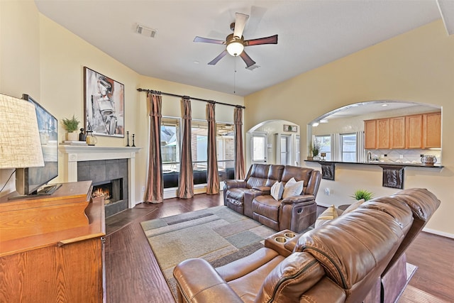 living room featuring visible vents, dark wood-type flooring, arched walkways, ceiling fan, and a tile fireplace