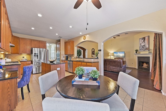 dining space featuring light tile patterned floors, recessed lighting, arched walkways, ceiling fan, and a tiled fireplace