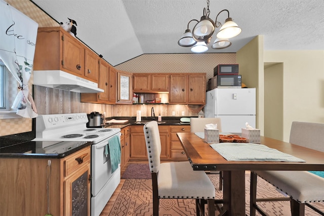 kitchen with under cabinet range hood, white appliances, dark countertops, and a chandelier