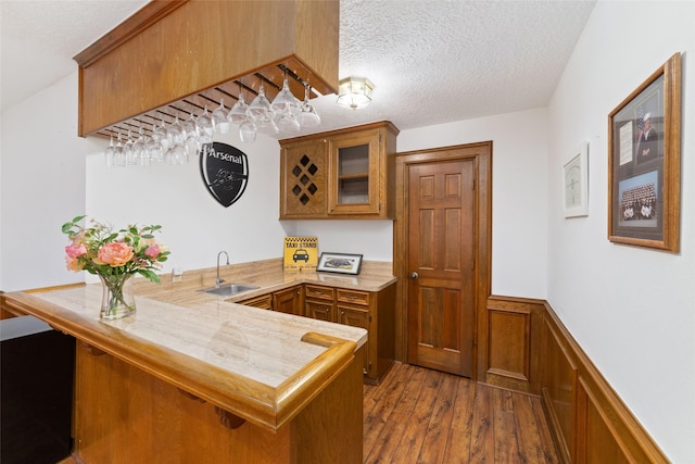 kitchen with a sink, a wainscoted wall, a peninsula, and brown cabinetry