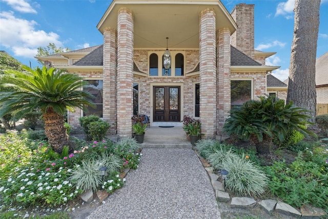 entrance to property featuring french doors, brick siding, a chimney, and a shingled roof