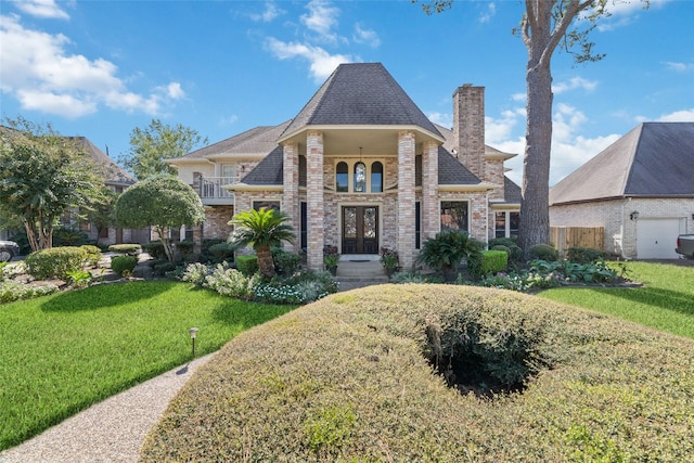 french country inspired facade featuring brick siding, french doors, a chimney, and a front yard