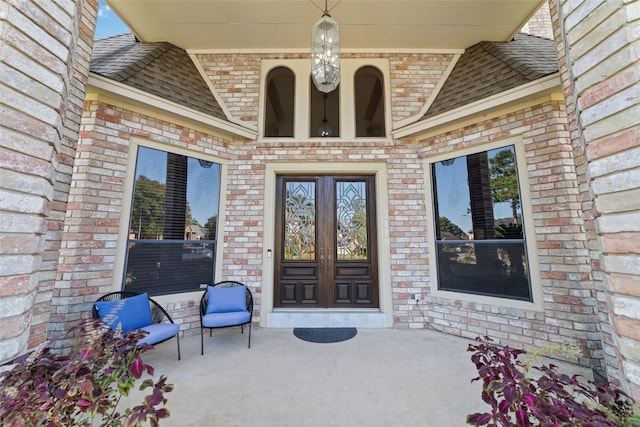 entrance to property featuring brick siding and roof with shingles