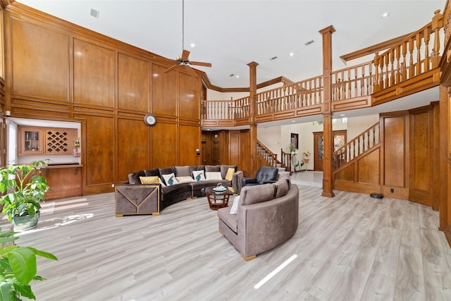 living area with a ceiling fan, stairway, a high ceiling, wood walls, and light wood finished floors