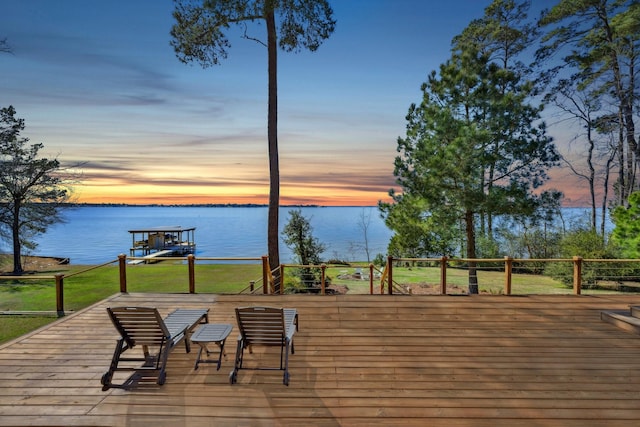 deck at dusk with a lawn, a water view, and a boat dock