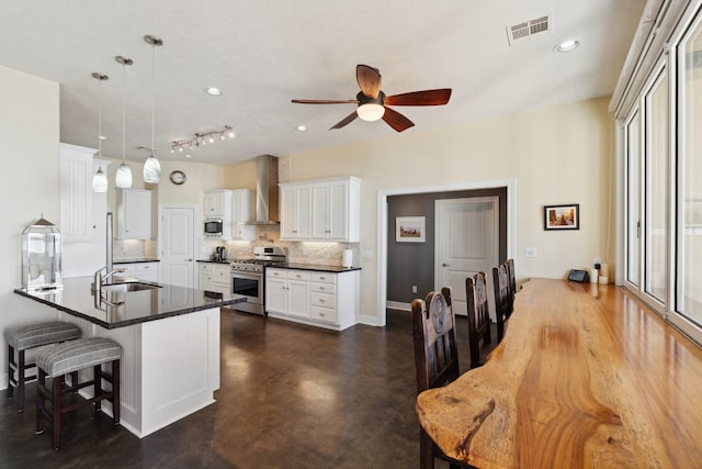 kitchen featuring visible vents, dark countertops, appliances with stainless steel finishes, a breakfast bar area, and wall chimney range hood