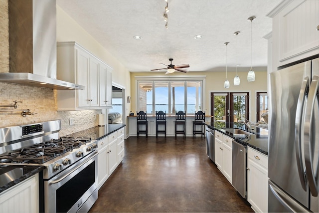 kitchen with concrete floors, ceiling fan, a sink, appliances with stainless steel finishes, and wall chimney range hood