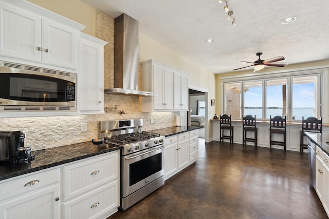 kitchen with ceiling fan, stainless steel appliances, white cabinetry, wall chimney range hood, and tasteful backsplash
