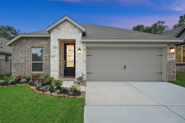 view of front facade with a front lawn, stone siding, concrete driveway, a shingled roof, and a garage