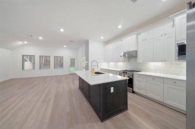 kitchen with a sink, light countertops, under cabinet range hood, stainless steel gas range oven, and tasteful backsplash