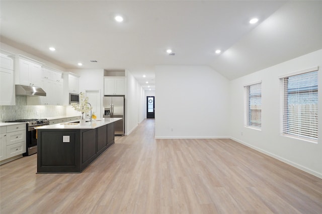 kitchen with under cabinet range hood, light wood-type flooring, light countertops, appliances with stainless steel finishes, and a kitchen island with sink