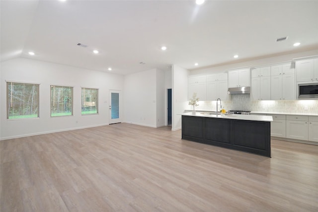 kitchen with a sink, decorative backsplash, light countertops, under cabinet range hood, and stainless steel microwave