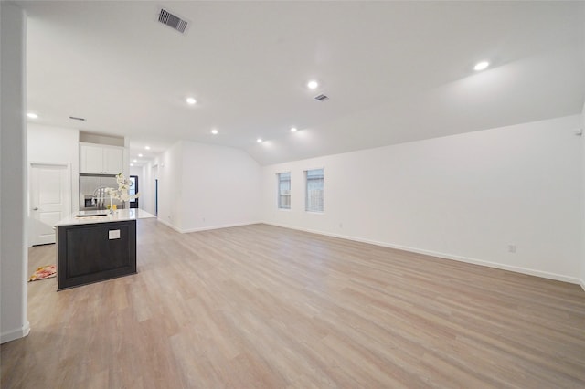 unfurnished living room with visible vents, light wood-style flooring, recessed lighting, a sink, and vaulted ceiling