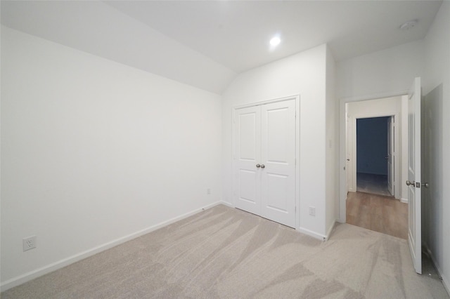 unfurnished bedroom featuring light carpet, a closet, lofted ceiling, and baseboards