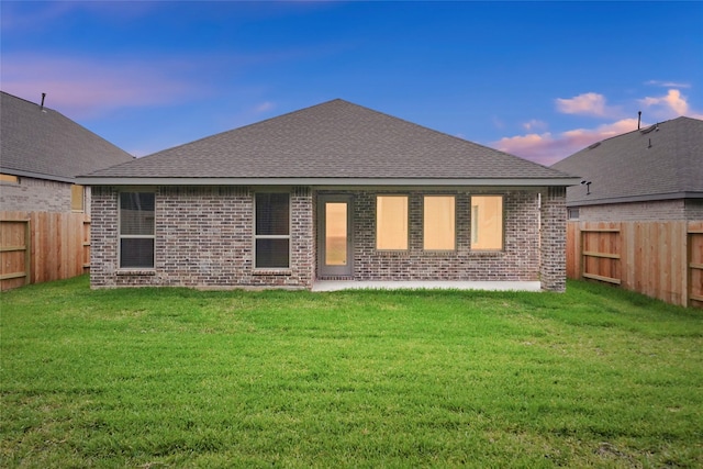 back of property at dusk with a lawn, brick siding, and a fenced backyard