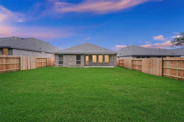 back of house at dusk featuring a yard, a fenced backyard, and brick siding