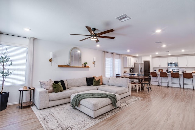 living area featuring a ceiling fan, plenty of natural light, light wood-style floors, and visible vents