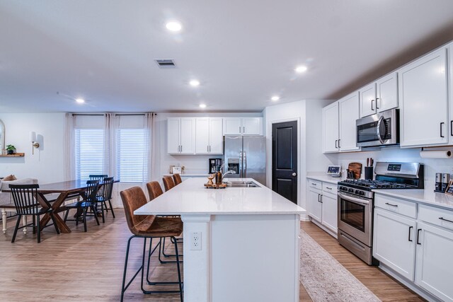 kitchen featuring a breakfast bar, an island with sink, recessed lighting, light wood-style floors, and stainless steel appliances