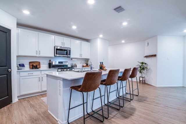 kitchen with light wood-type flooring, visible vents, a breakfast bar, a sink, and stainless steel appliances