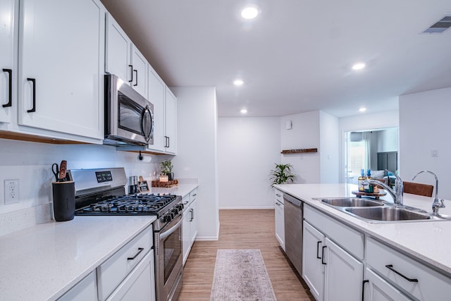 kitchen with recessed lighting, appliances with stainless steel finishes, light wood-style floors, white cabinetry, and a sink