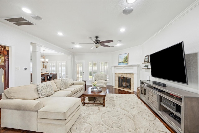 living room with visible vents, dark wood finished floors, a tiled fireplace, crown molding, and ceiling fan with notable chandelier