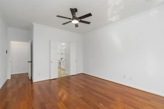 unfurnished bedroom with a ceiling fan, wood finished floors, baseboards, crown molding, and connected bathroom