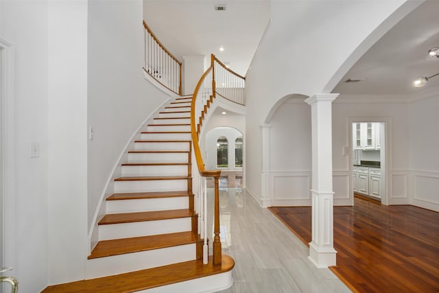 stairway with wood finished floors, decorative columns, arched walkways, ornamental molding, and a decorative wall