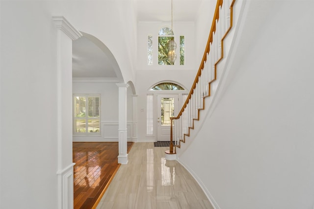 entryway featuring arched walkways, light wood-type flooring, a wealth of natural light, and ornamental molding