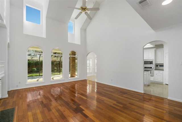 unfurnished living room featuring hardwood / wood-style flooring, arched walkways, visible vents, and ceiling fan