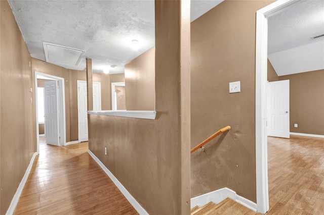 corridor with light wood finished floors, baseboards, attic access, an upstairs landing, and a textured ceiling